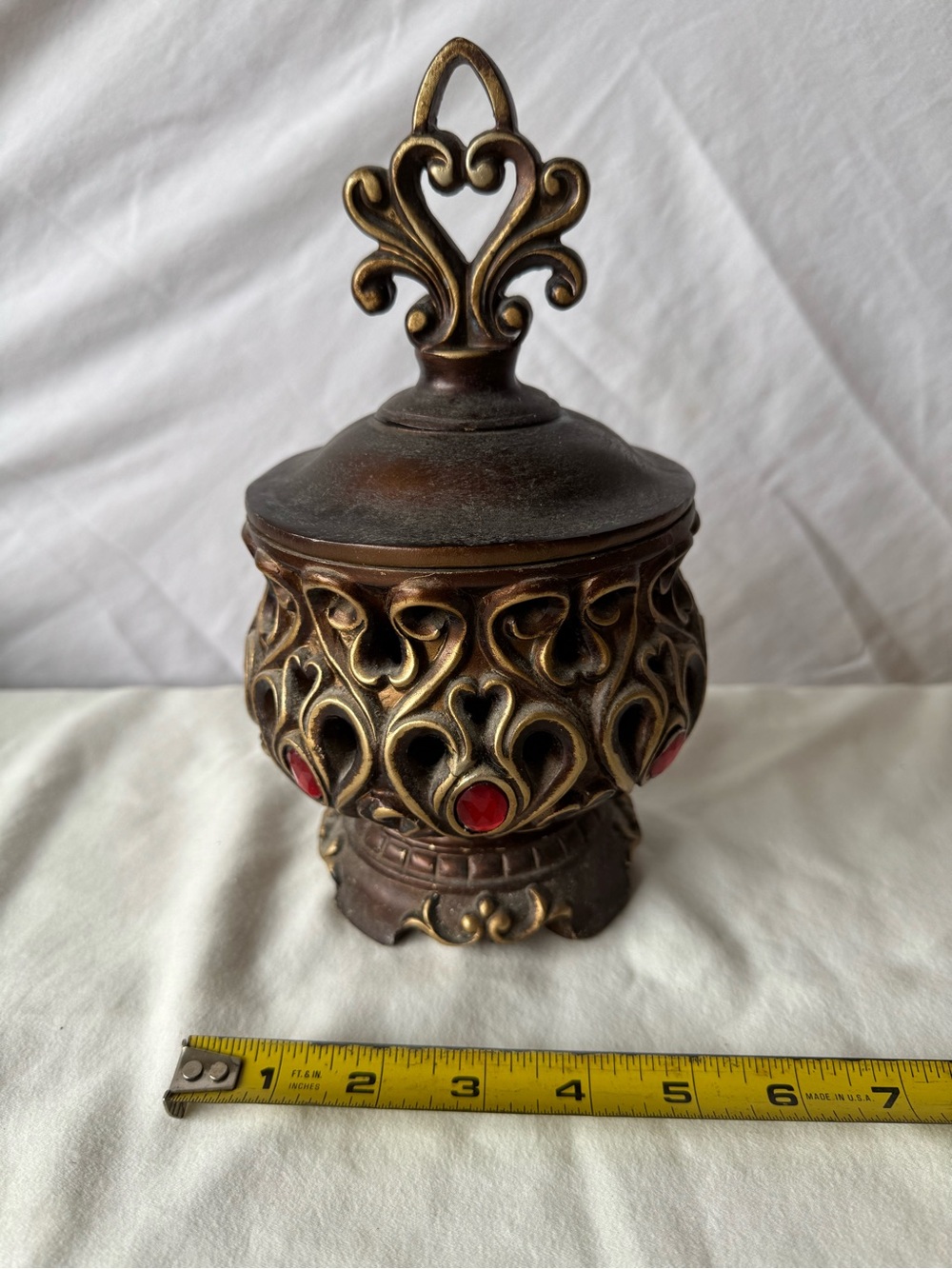 resin decorative lidded jar with openwork scrollwork and red faux-gem accents.